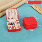 Red jewelry box with compartments containing jewelry items on a blue surface.