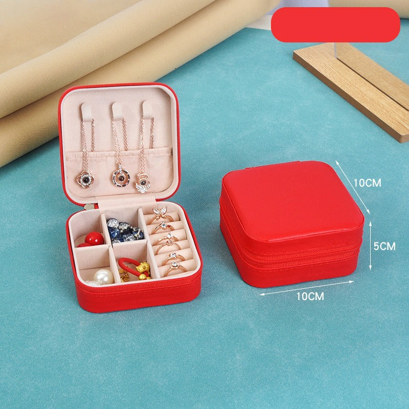 Red jewelry box with compartments containing jewelry items on a blue surface.