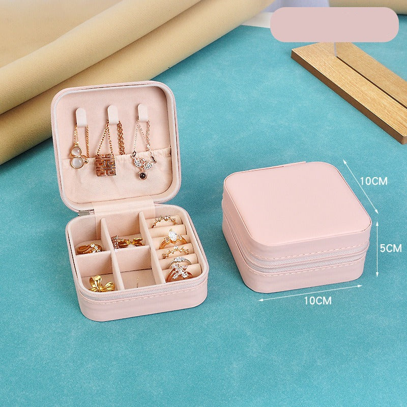 Pink jewelry box with compartments filled with jewelry on a blue surface, with dimensions indicated.