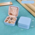 Blue jewelry box with compartments filled with jewelry on a teal surface, with dimensions indicated.
