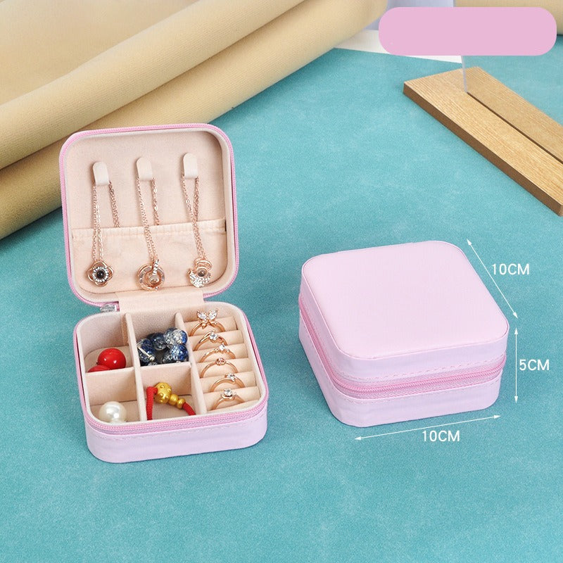 Pink jewelry box with compartments containing jewelry on a blue surface