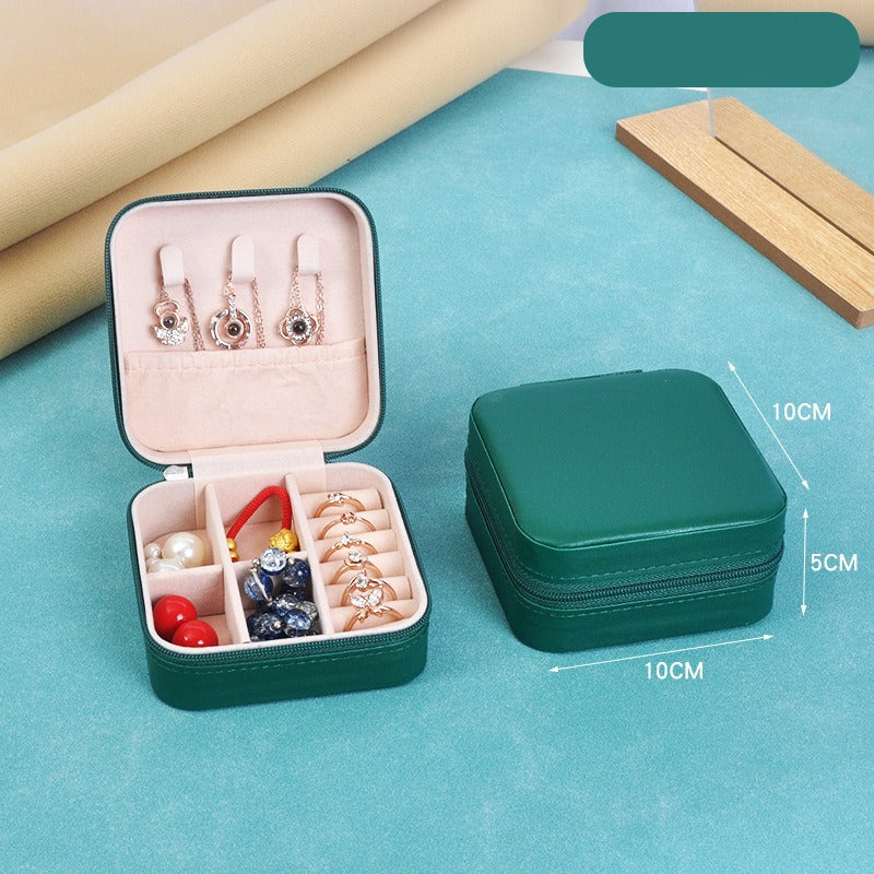Green jewelry case with open lid displaying earrings and accessories on a blue surface.